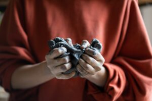 Close-up of woman hands in red sweater kneading sculptural clay intended for making figurines