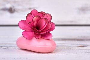 Close-up pink soap with rose flower head on white wood.