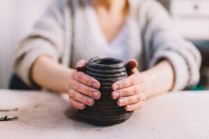 Crop hands making clay pot