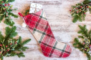 Holiday flat lay with plaid Christmas stocking and pine branches